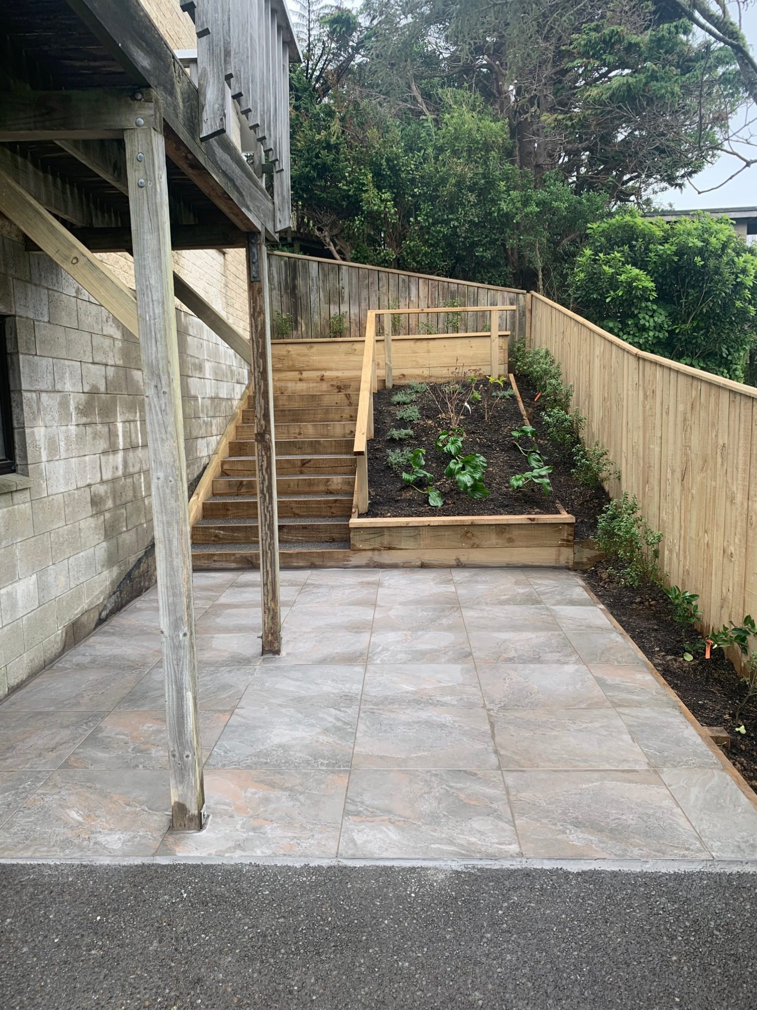 A freshly laid tiled patio with timber retaining and a handrail, finished on a Wellington build