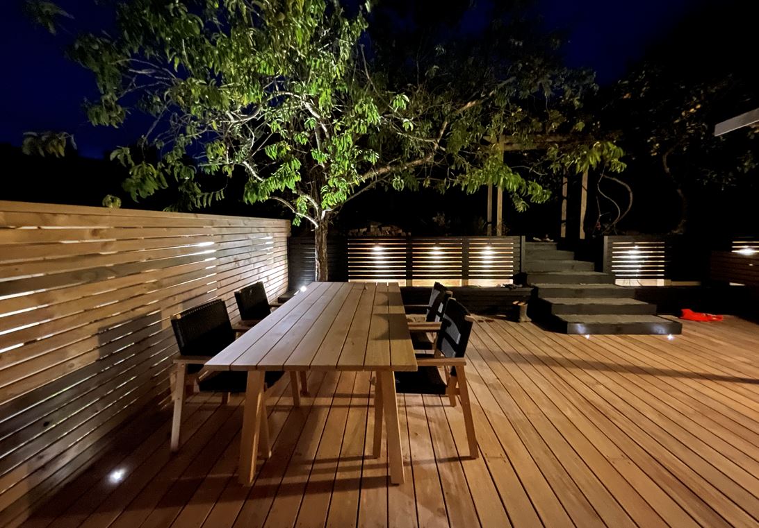 Night-lit timber deck with outdoor dining and a slatted privacy screen
